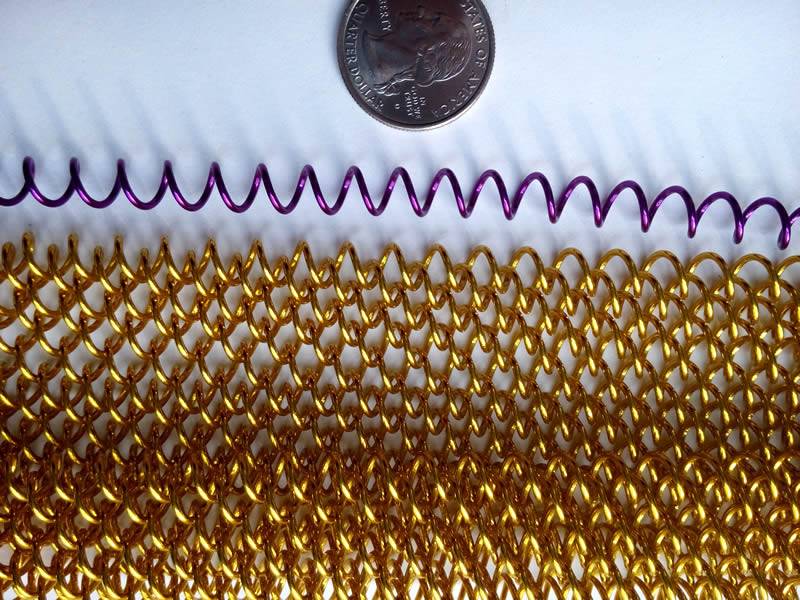 A piece of golden color coil fabric and a piece of purple coil wire are beside a metal coin.