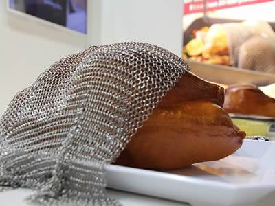 A piece of stainless steel chainmail baking cover is covering a chicken in the plate.