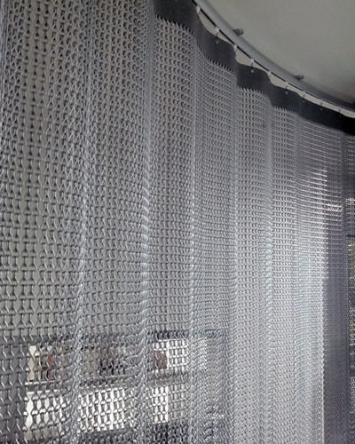 Anodized chain link curtain is installed forming pleated shape at room for a divider